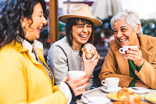 Three ladies sitting around a small table laughing and drinking coffee