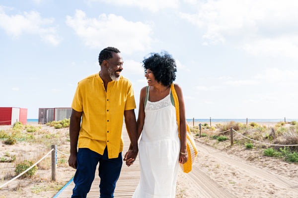 A couple holding hands while walking on a boardwalk on the beach